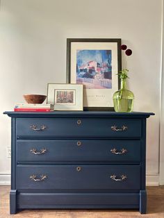 a blue dresser with some pictures on top and a green vase sitting on top of it