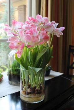 pink tulips are in a glass vase on a table next to a window