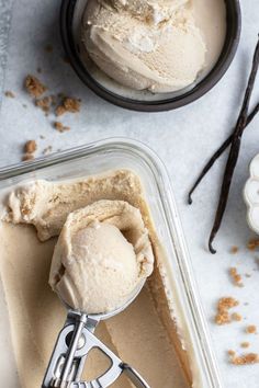 two scoops of ice cream sitting in a container with spoons next to it