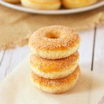 three donuts stacked on top of each other in front of a plate of doughnuts