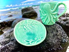 two ceramic cups sitting on top of a rock near the ocean