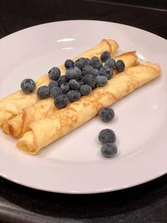 crepes with blueberries and syrup are on a white plate, ready to be eaten