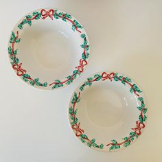 two white bowls with red bows and green leaves on them sitting next to each other