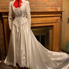 a white wedding dress on display in front of a fire place with a red ribbon