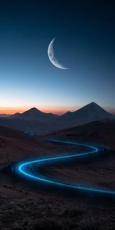 a long winding road in the desert at night with a crescent shaped moon above it