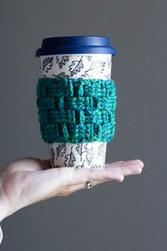 a hand holding a coffee cup covered in green crocheted yarn and a blue lid