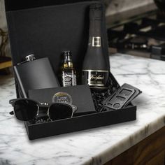 an assortment of men's personal care items on a marble countertop in a black box