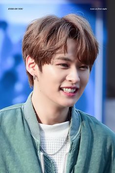 the young man is smiling while wearing a green jacket and white t - shirt with an earring