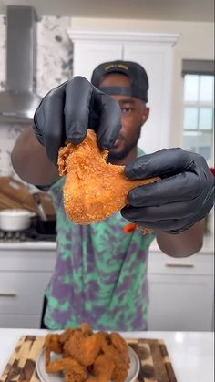 a man in black gloves holding up a piece of fried chicken to the camera with his hands