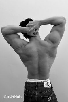 a shirtless man with his back to the camera, holding his hands behind his head