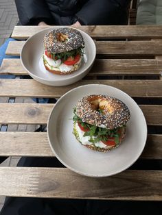 two bagels with cheese, lettuce and tomato on them sitting on a wooden table