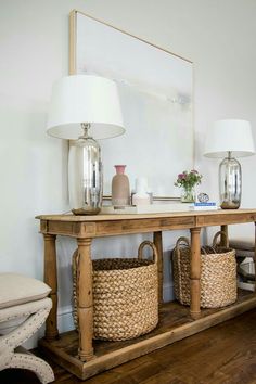 a wooden table with baskets under a mirror and lamps on it's sideboard