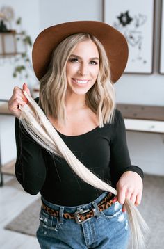 a woman with long blonde hair wearing a brown hat and black shirt is smiling at the camera