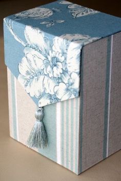 a blue and white striped box with flowers on the front, tassels hanging from it