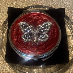 a red compact with a butterfly design on the front in a clear plastic case sitting on a table