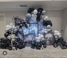 a table topped with black and white balloons, skeleton decorations and a sign that says let's party