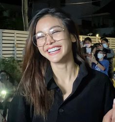 a woman wearing glasses and smiling at the camera with people in the background taking pictures