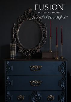 a black dresser with candles and a mirror on it's top, in front of a dark wall