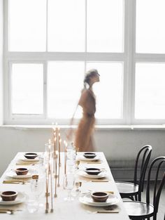 a woman walking past a table with plates and candles on it