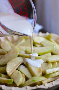 someone is pouring milk on apples in a pie crust