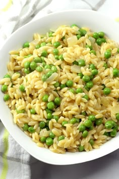 a bowl filled with pasta and peas on top of a white table cloth next to a fork