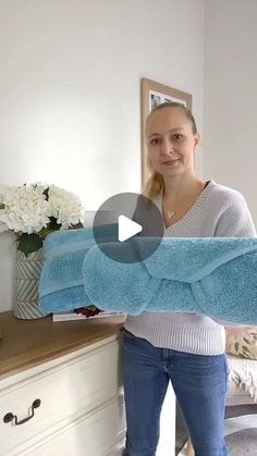 a woman standing in front of a bed holding a blue towel