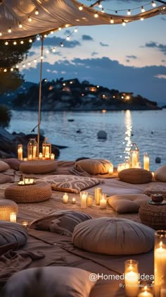 candles are lit on the ground next to some pillows and blankets with lights hanging from them