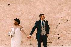 a bride and groom holding hands in front of a wall