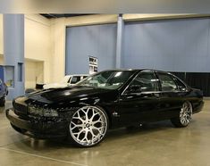 a black car parked in a garage next to two other cars on the floor and one has chrome rims