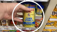 a hand holding a can of corn starch in front of a store display shelf