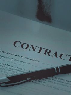 a pen sitting on top of a paper with the word contract written in black and white