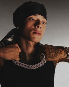 a man with tattoos on his arm and wearing a black tank top holding onto a chain