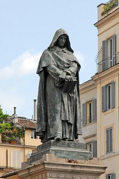 a statue of a person with a hood and cape standing in front of a building