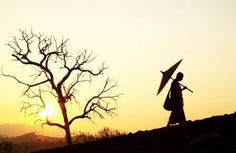 a person holding an umbrella walking on a hill with the sun setting in the background