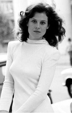 black and white photograph of a woman standing in front of a car wearing a turtle neck sweater