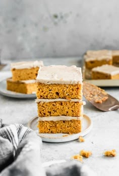 a stack of carrot cake with frosting on a white plate next to two forks