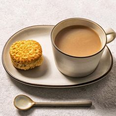 a cup of coffee next to a biscuit on a plate