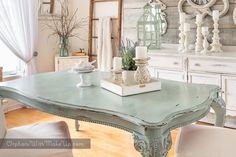 a dining room table with white chairs and an old clock on the wall behind it