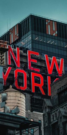 the word new york is lit up in red on top of a building near other buildings