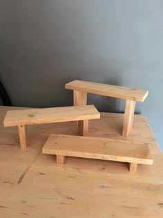 three wooden benches sitting on top of a wooden table next to a gray painted wall