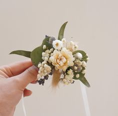 a hand holding a flower bouquet with white and yellow flowers on the top of it