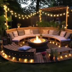 an outdoor fire pit surrounded by wooden benches and seating area with lights strung around it