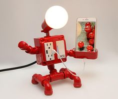 a red robot holding a cell phone and plugged in to it's socket