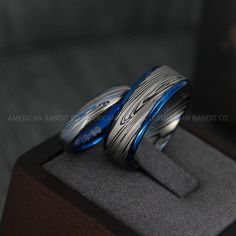 two wedding bands are sitting on top of a wooden display case in front of a black background