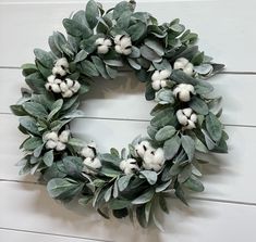 a wreath is hanging on the wall with cotton balls and eucalyptus leaves in front of it