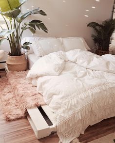 a bed with lots of pillows and blankets on it in a room filled with plants