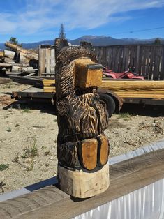 a wooden statue sitting on top of a cement slab next to a pile of wood