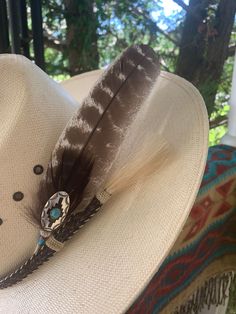 Feather consist of turkey wing feather;  measuring from feather tip to quill end 9.25 inches long.  Accented with small turkey down feather and turquoise Indian style medallion.   Quill is wrapped in natural deer backstrap for strength and durability.  Simple, statement piece with a pop of color that's sure to  add extra dimension to your western attire. All hat feathers are designed and hand created by me.    Feathers are packed in proper packaging appropriate for feathers to ensure its safe arrival. Note: feathers are ethically sourced.   Hat for display purpose only. Southwestern Brown Feather Hat Bands, Southwestern Brown Hat Bands With Feathers, Southwestern Feather Hat Band For Country Events, Southwestern Style Hats With Feathers For Rodeo, Southwestern Hat With Feathers For Rodeo, Southwestern Feathered Hats For Rodeo, Southwestern Style Feathered Hats For Rodeo, Southwestern Brown Hat With Feathers, Southwestern Style Hats With Feathers For Ranch