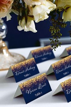 there are place cards on the table with flowers in the vase behind them and gold confetti