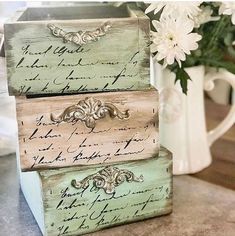 three wooden boxes sitting on top of a counter next to a vase with flowers in it